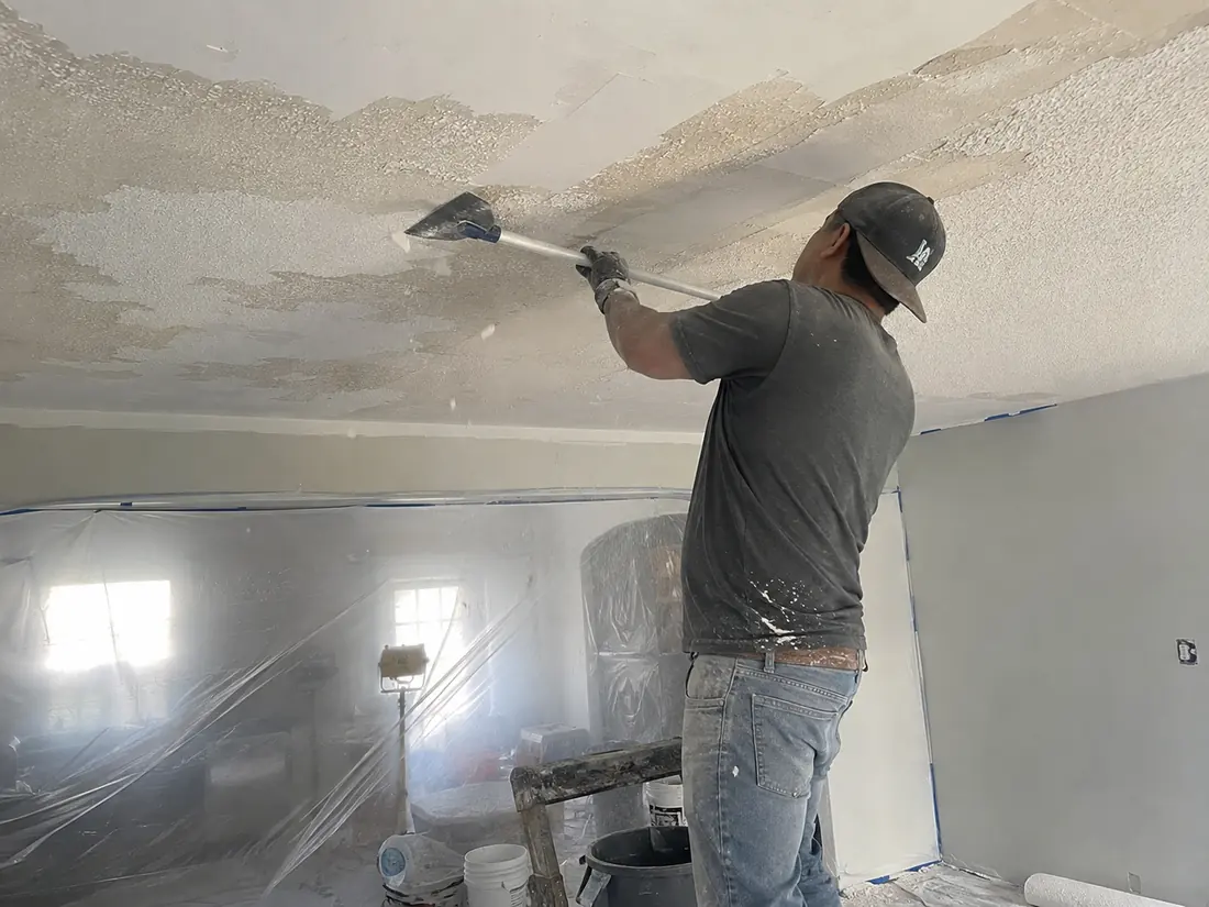Popcorn ceiling texture being scraped from a ceiling